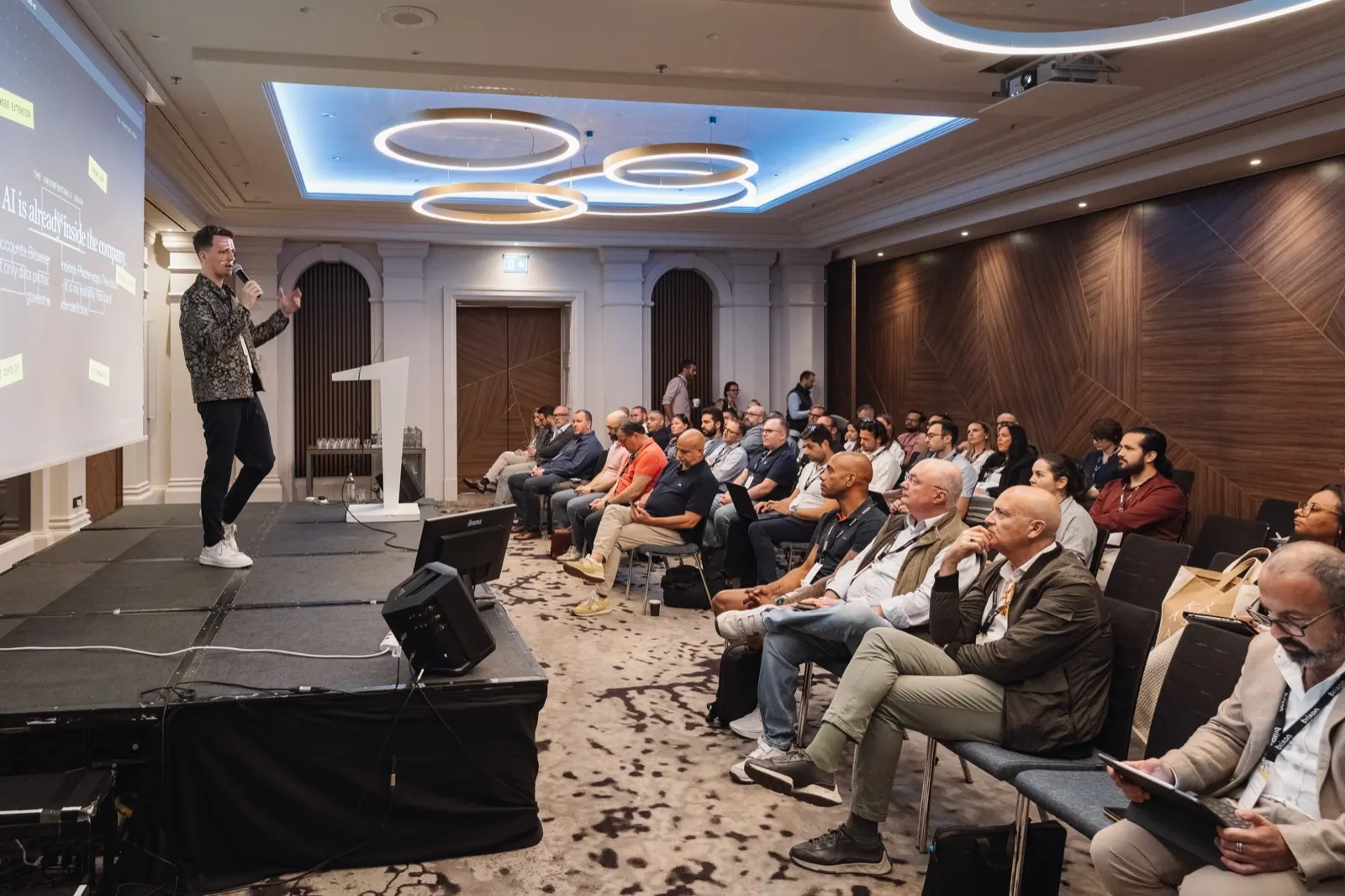 Christoph Sauerborn speaking to a seated audience, slide reading “AI is already inside the company”.